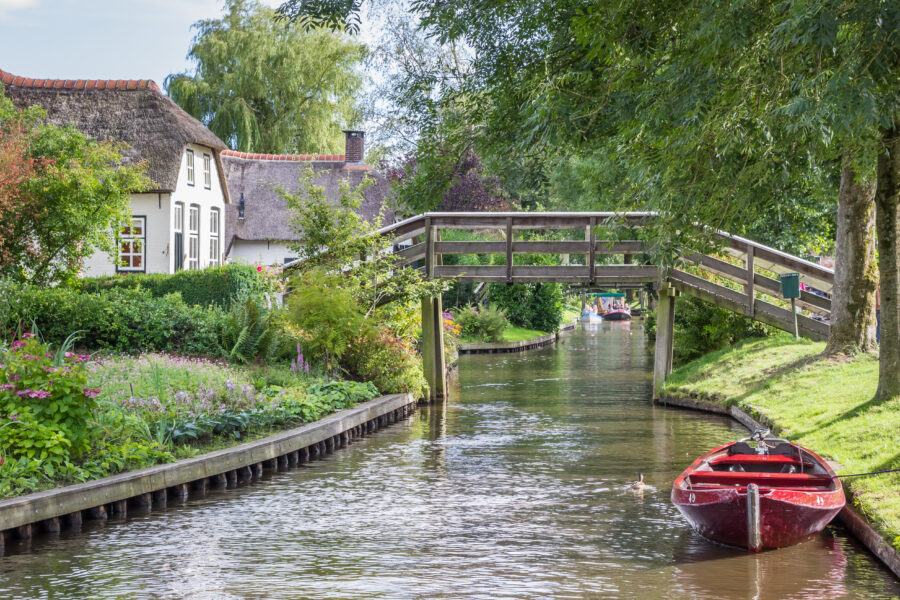 Traditional red punter boat gliding through Giethoorn's canals, surrounded by thatched-roof houses and scenic historic views