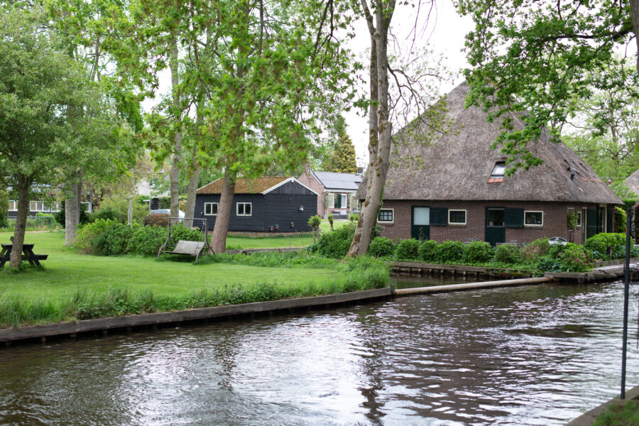 Giethoorn village in the Netherlands, showcasing a canal, traditional homes, and a tourist woman admiring the skyline.