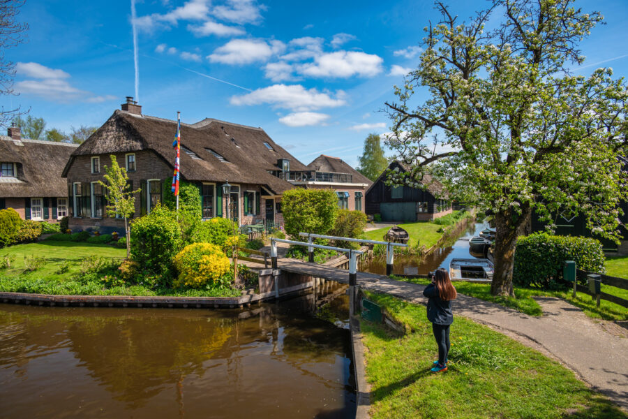 Scenic view of Giethoorn, Netherlands, featuring a canal, traditional houses, and a tourist woman exploring the village.