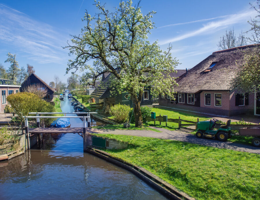 Scenic view of Giethoorn, Netherlands in spring, featuring lush greenery and charming canals lined with quaint houses.
