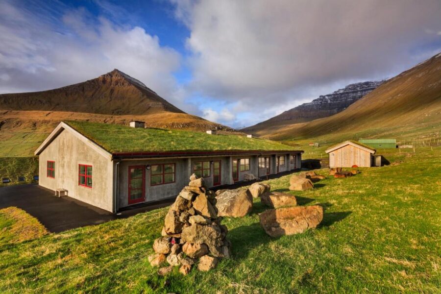 Gjaargardur Guesthouse Gjogv surrounded by lush grass and majestic mountains in the Faroe Islands.