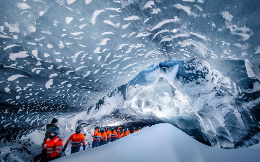 Adventurers in bright jackets exploring a breathtakingly vast icy cave with stunning formations.