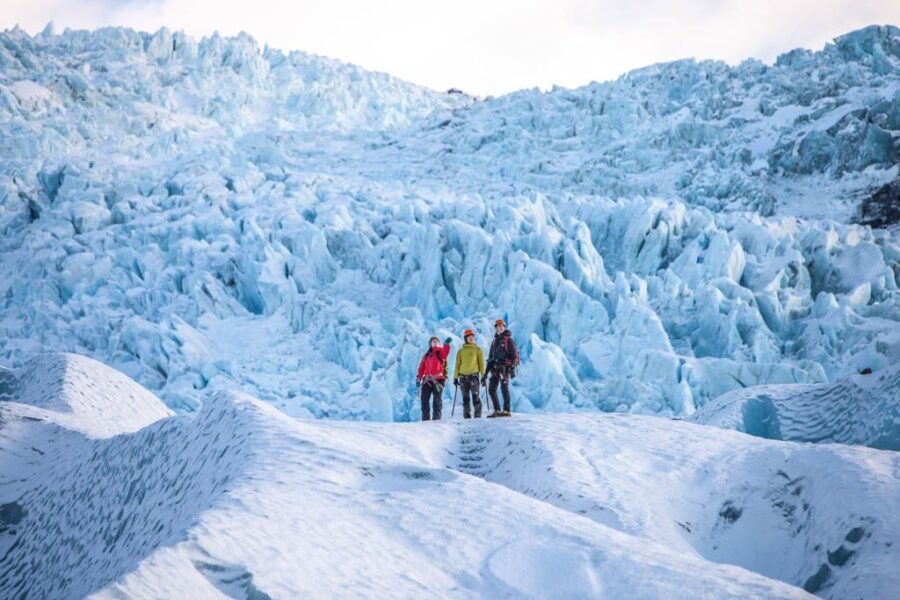 Climbers on a vast glacier under blue sky, showcasing icy landscapes and adventure.