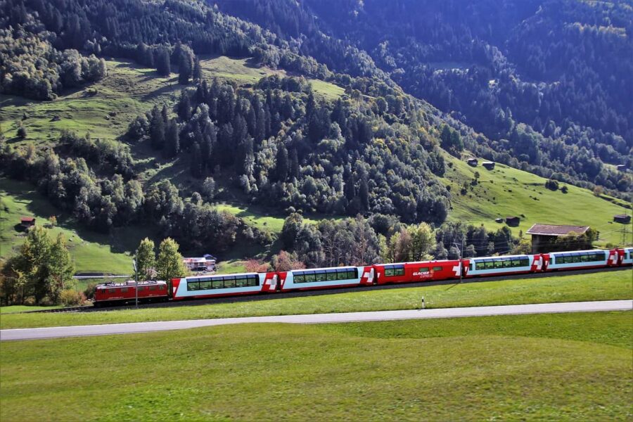 Swiss train traverses scenic green landscape with rolling hills and forests.