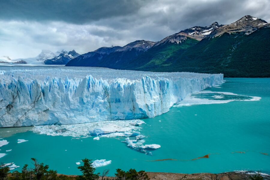 Dramatic Patagonia glacier, turquoise lake and snow-capped mountains under stormy clouds scenic landscape.