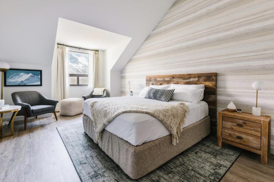 Interior of a Glacier View Lodge bedroom in Canada, showcasing a bed, a chair, and a window with scenic views.