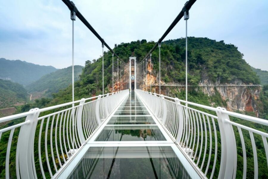 Stunning glass suspension bridge above lush landscape with mountains, forests, and modern design.