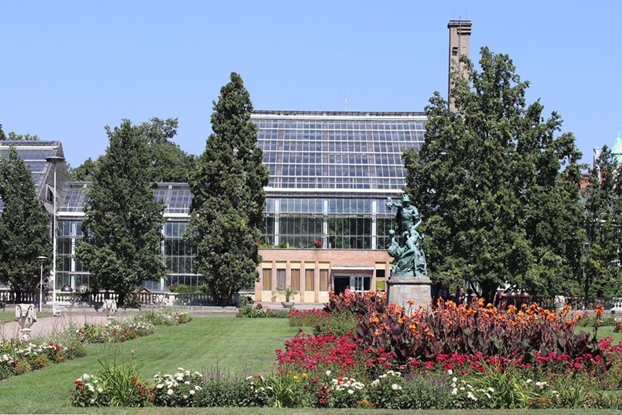 Poznań Palm House conservatory with formal garden, lawn, and bronze statue.
