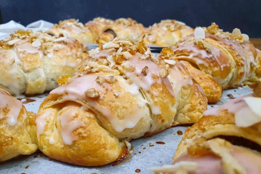 Freshly baked glazed almond croissants, flaky buttery pastries topped with icing and sliced almonds.