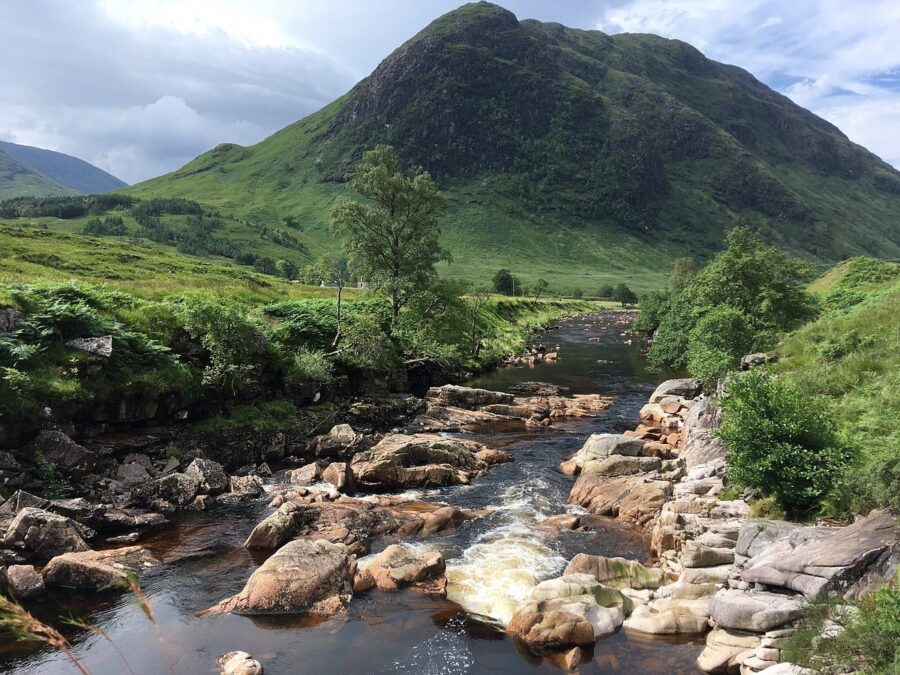 Scenic view of a river winding through rocky terrain, with majestic mountains behind, located in Glencoe Village, Scotland