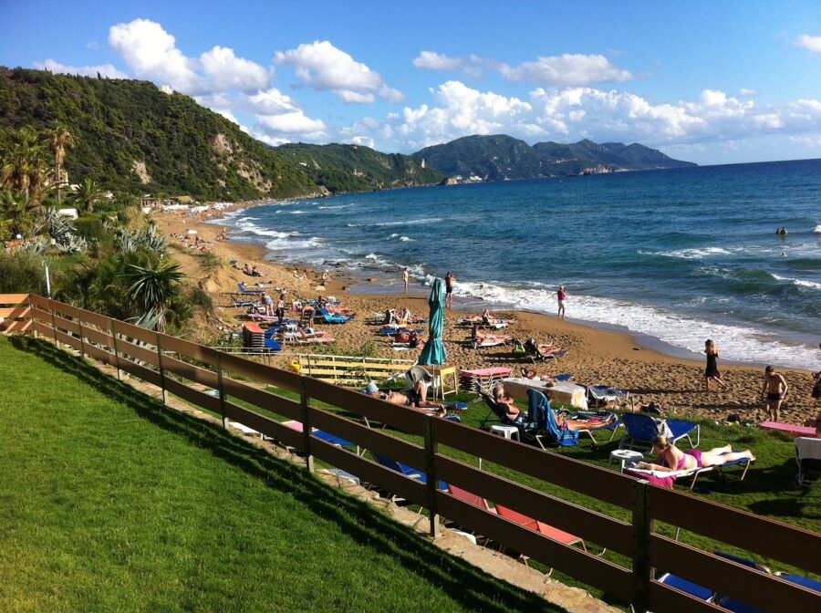 Sunny Glyfada Beach: sandy shore, lush hills, vibrant crowd enjoying leisure and ocean waves.