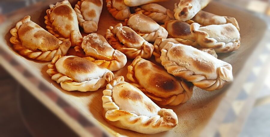Freshly baked golden-brown empanadas in a rustic wooden tray, showcasing crisp textures and handmade detailing.