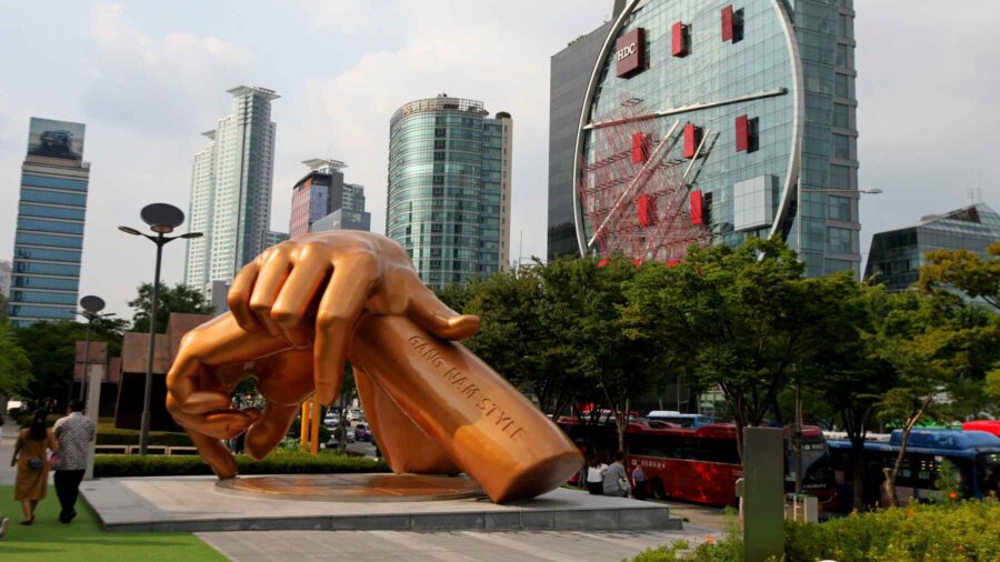 Golden hand sculpture in urban Gangnam featuring Gangnam Style surrounded by skyscrapers and greenery.