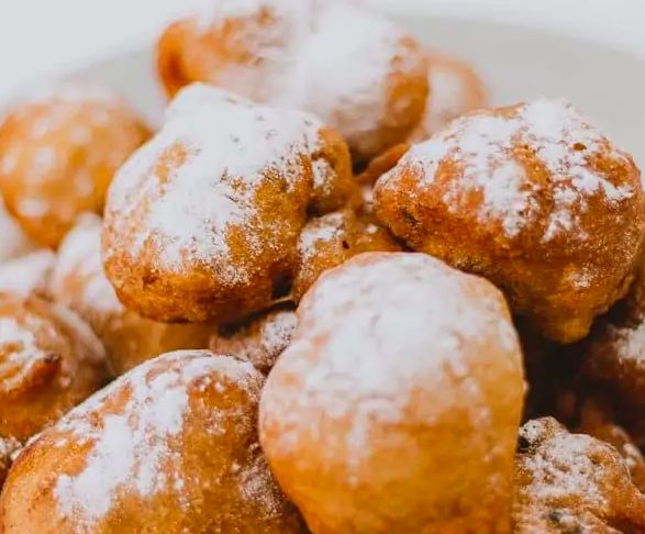 Golden brown oliebollen with powdered sugar, crispy exterior, fluffy interior, delightful fried pastries.