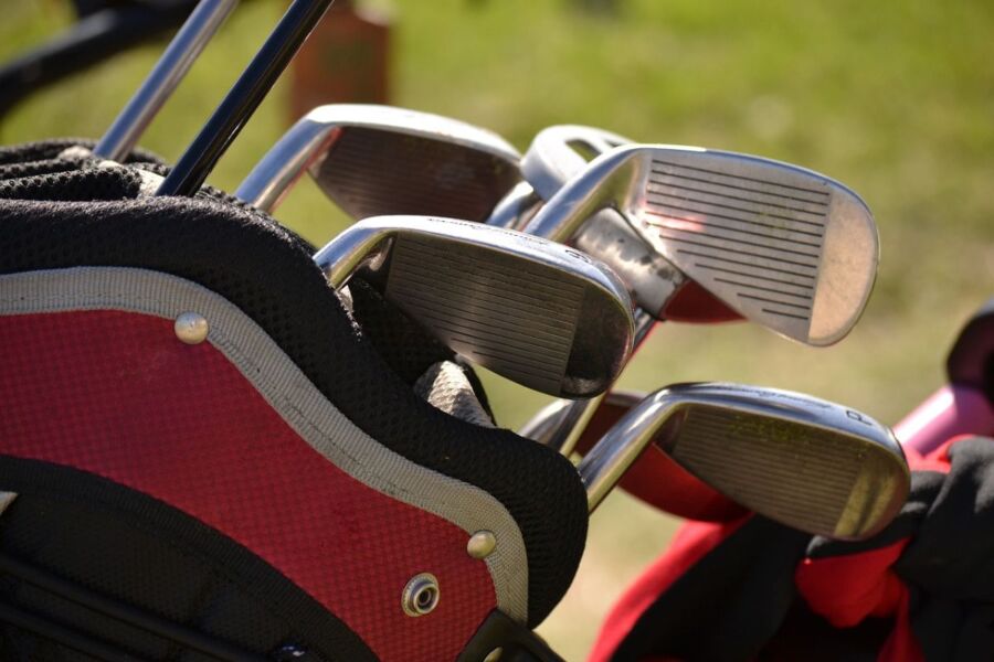 Red and black golf bag with clubs on lush green grass, highlighting premium golfing equipment.