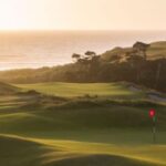 Scenic golf course at coastal sunset with lush greens and tranquil sea view.