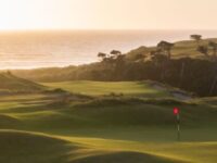 Scenic golf course at coastal sunset with lush greens and tranquil sea view.