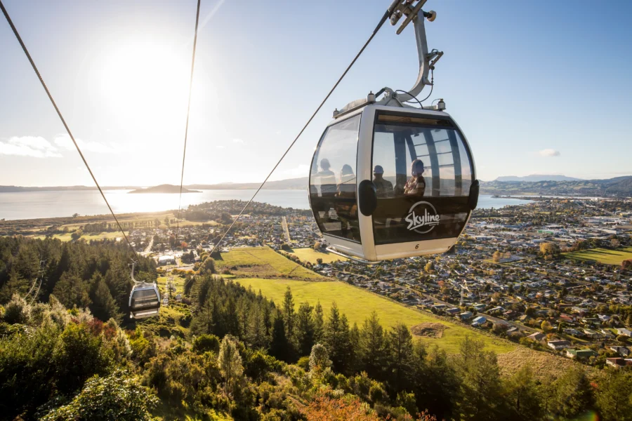 Skyline Rotorua gondola gliding above forested hillside, overlooking lakeside town and distant mountains.