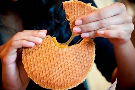 Hands pulling apart gooey caramel stroopwafel, melted filling stretching in cozy indoor setting.