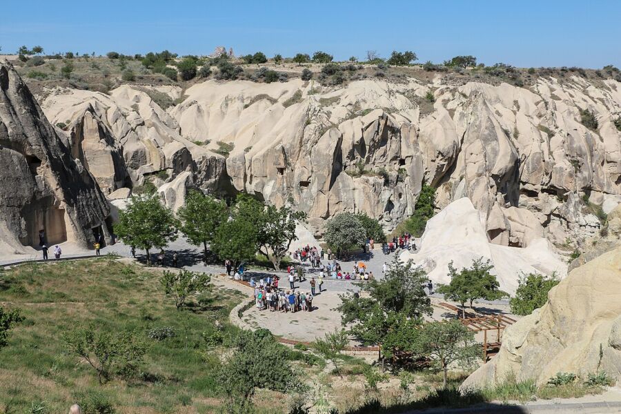 Visitors walking on a path beside a cliff at the Göreme Open-Air Museum, enjoying the unique landscape and historical site.