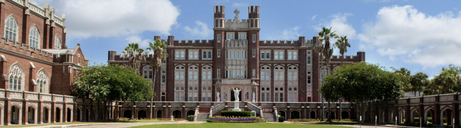 Grand historical university building with red brick facade, gothic windows, spires, and manicured lawn.
