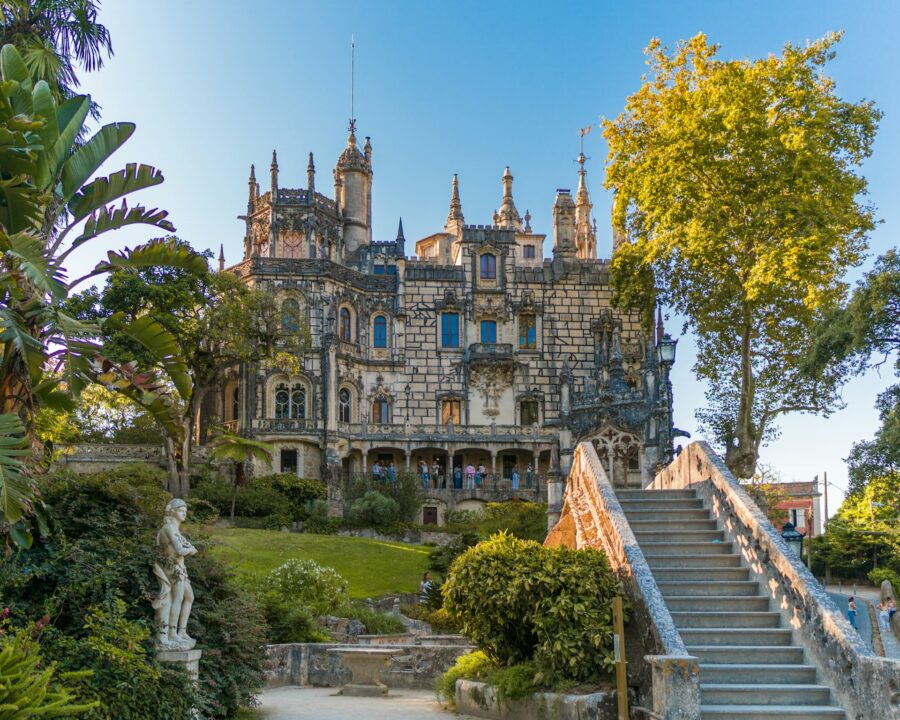Gothic-style castle with spires, balconies, garden, and visitors enjoying historic architecture.