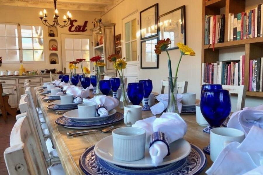 Long dining table elegantly set with blue glasses, white napkins, and plates, adorned with vibrant flowers in vases on a Gourmet Brunch in Charming Santa Fe with Chef Carolina. 