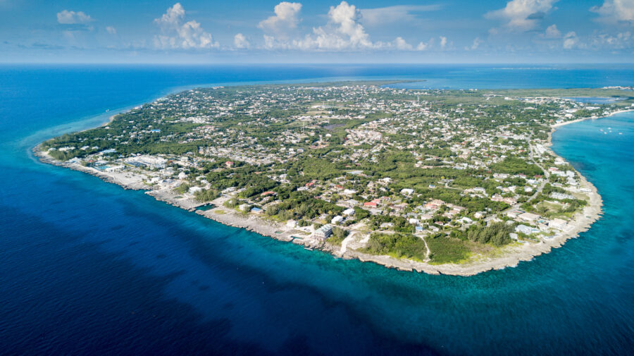 Aerial view of Grand Cayman, with the island and the extensive coral reef visible in the crystal-clear waters. 
