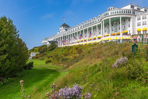 Historic white hilltop resort hotel with grand porch, American flags, green lawn, and blue sky.