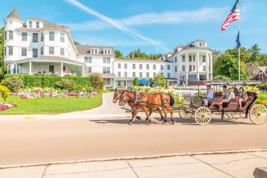 Historic island hotel with horse-drawn carriage, summer gardens, American flag, and waterfront resort ambiance.