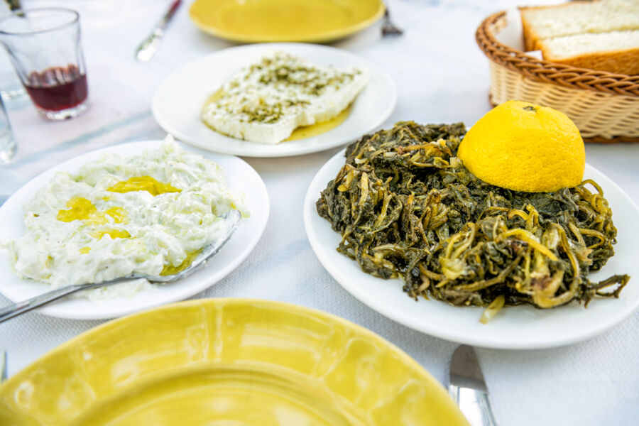 Horta wild greens topped with tzatziki, olive oil, and feta kathoura cheese, featured at a restaurant on Ikaria Island, Greece.