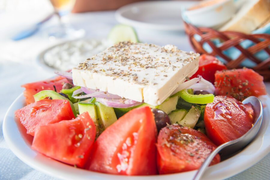 Greek feta salad with cucumbers and tomatoes, accompanied by tzatziki and bread in the background