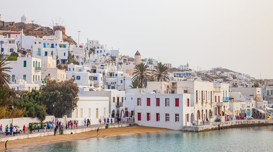 Picturesque Greek island village with whitewashed buildings and tranquil waterfront at sunset.