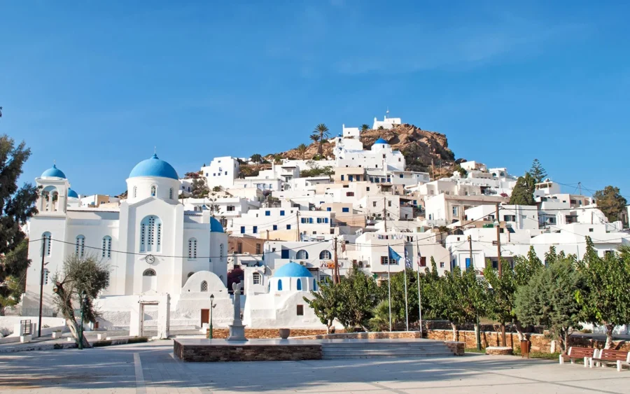 Picturesque Greek village with whitewashed buildings, blue domes, lush greenery, and Mediterranean charm.