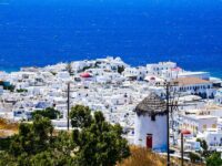 Picturesque Greek island coastal village with white architecture against blue sea and windmill scenery.