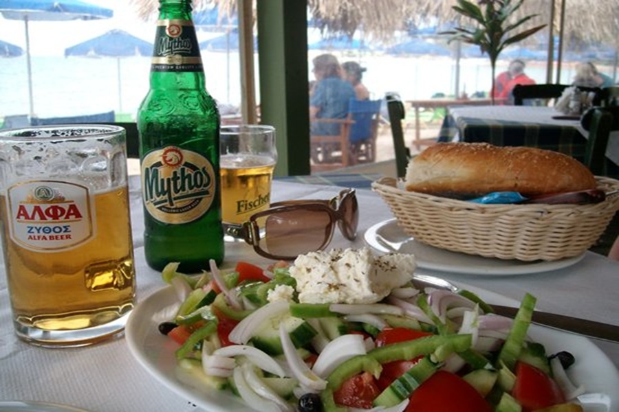 Greek salad and local beers on a beachside dining table.