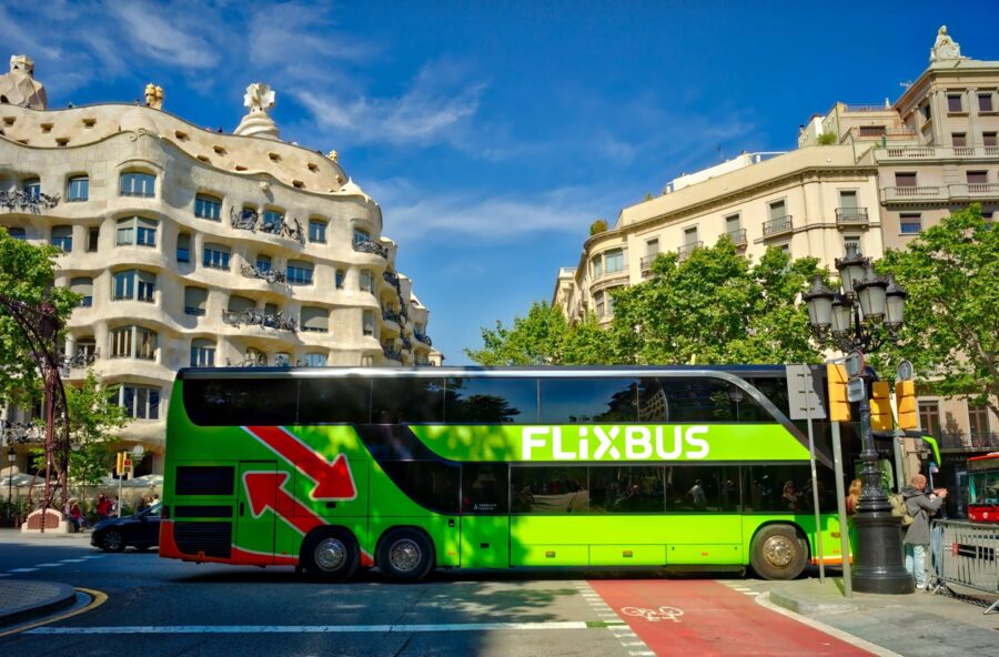Green FlixBus double-decker at city intersection with curving modernist limestone building.