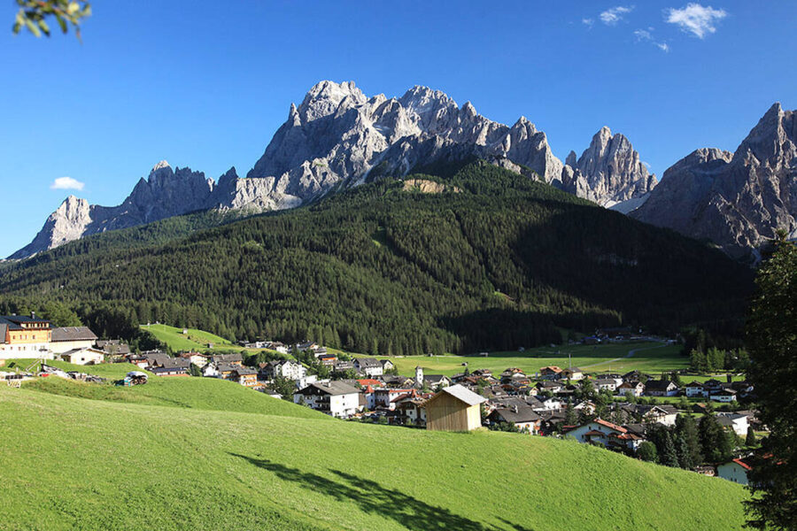 Dolomites Sexten mountain village with green meadow, wooden barn, forest and jagged peaks.