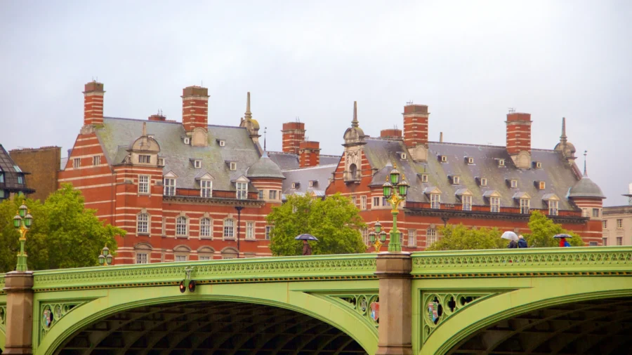 Green iron Westminster Bridge in London with red‑brick historic building and pedestrians.