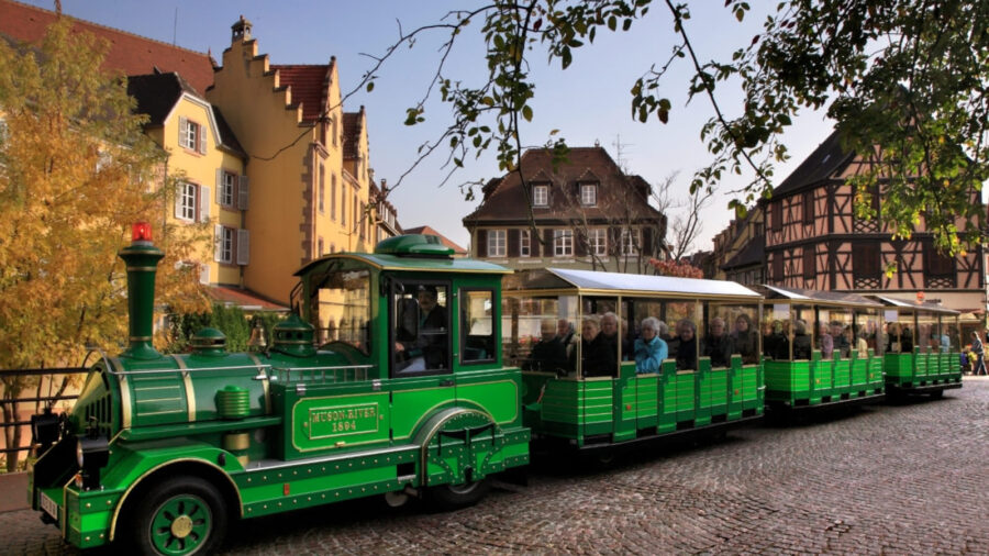 Colmar green tourist train on cobblestone street.