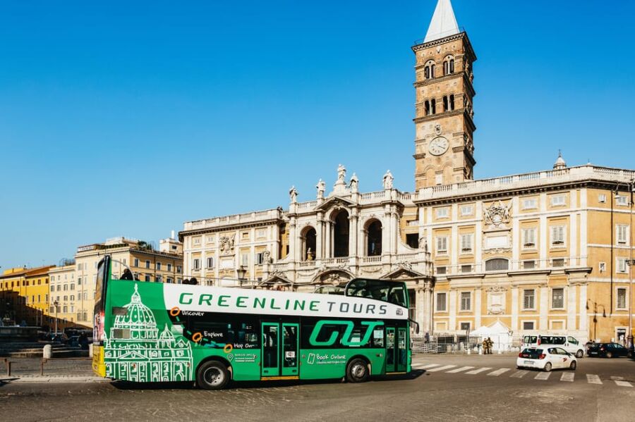 Tour bus at historical landmark with clock tower, columns, and sunny blue sky.