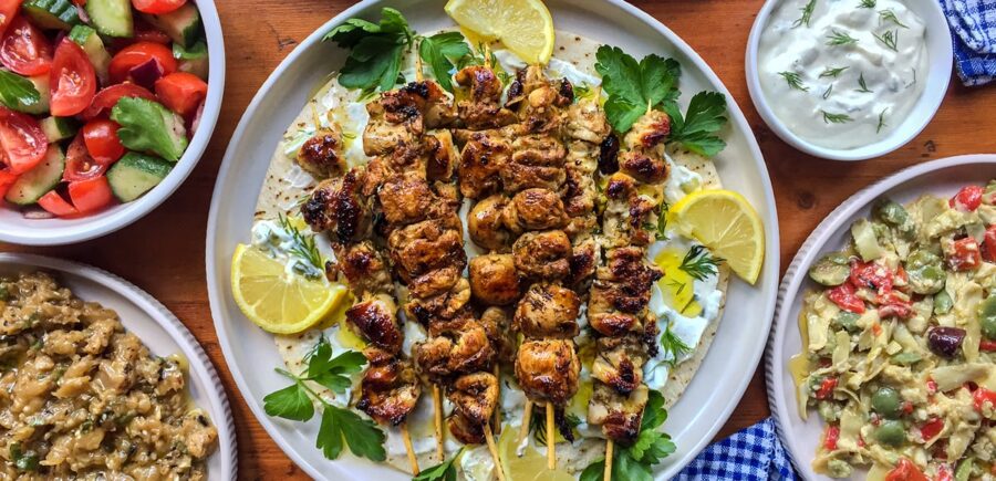 Mediterranean spread: grilled chicken skewers, fresh salad, creamy dips, vibrant vegetables.