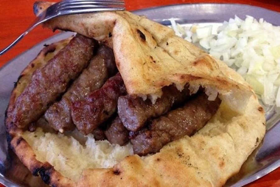 Traditional čevapi in flatbread with onions on a stainless steel plate.