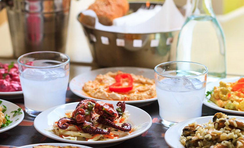 Mediterranean feast with grilled octopus, fresh salads, and local beverages on a rustic table.