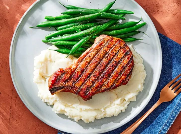 Grilled pork chop with mashed potatoes and green beans on a plate.