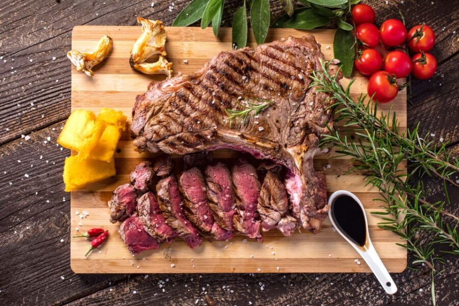 Beautifully grilled steak with rosemary, polenta, cherry tomatoes, and chili peppers on a wooden board.
