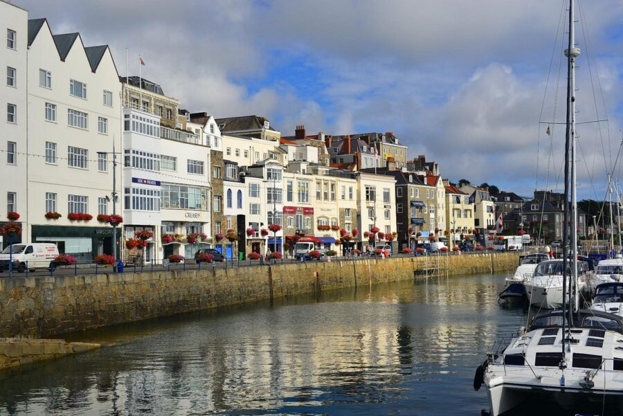 Calm water reflects buildings in Guernsey, United Kingdom, creating a serene coastal scene.
