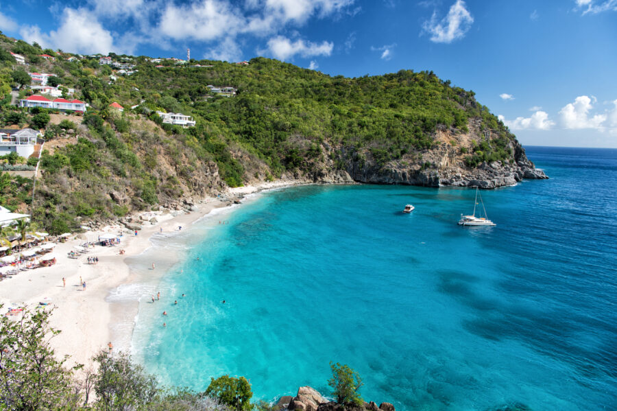 Scenic harbor with a sandy beach, blue sea, and mountains in Gustavia, St. Barts, evoking summer vacation vibes.