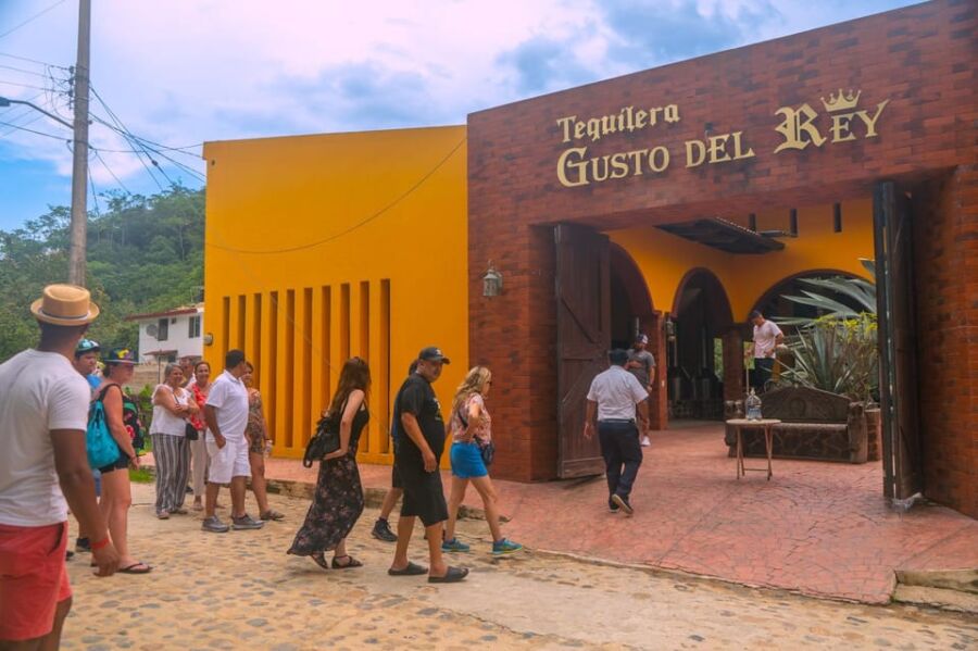 Tequila distillery entrance with tourists, vibrant facade, rustic charm, picturesque setting.