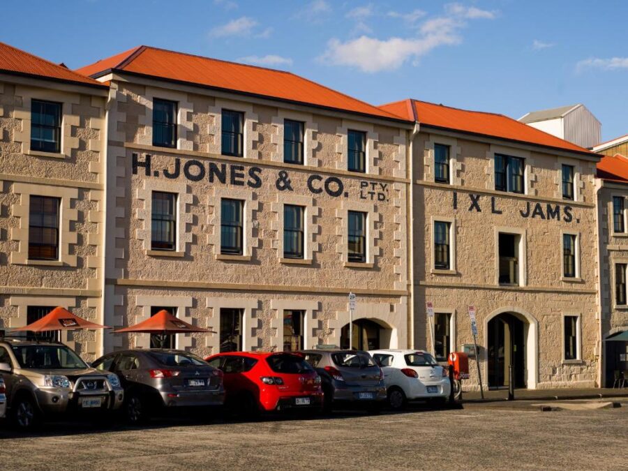 Historic Henry Jones IXL Jam Factory building in Hobart with stone facade, orange roof, parked cars.